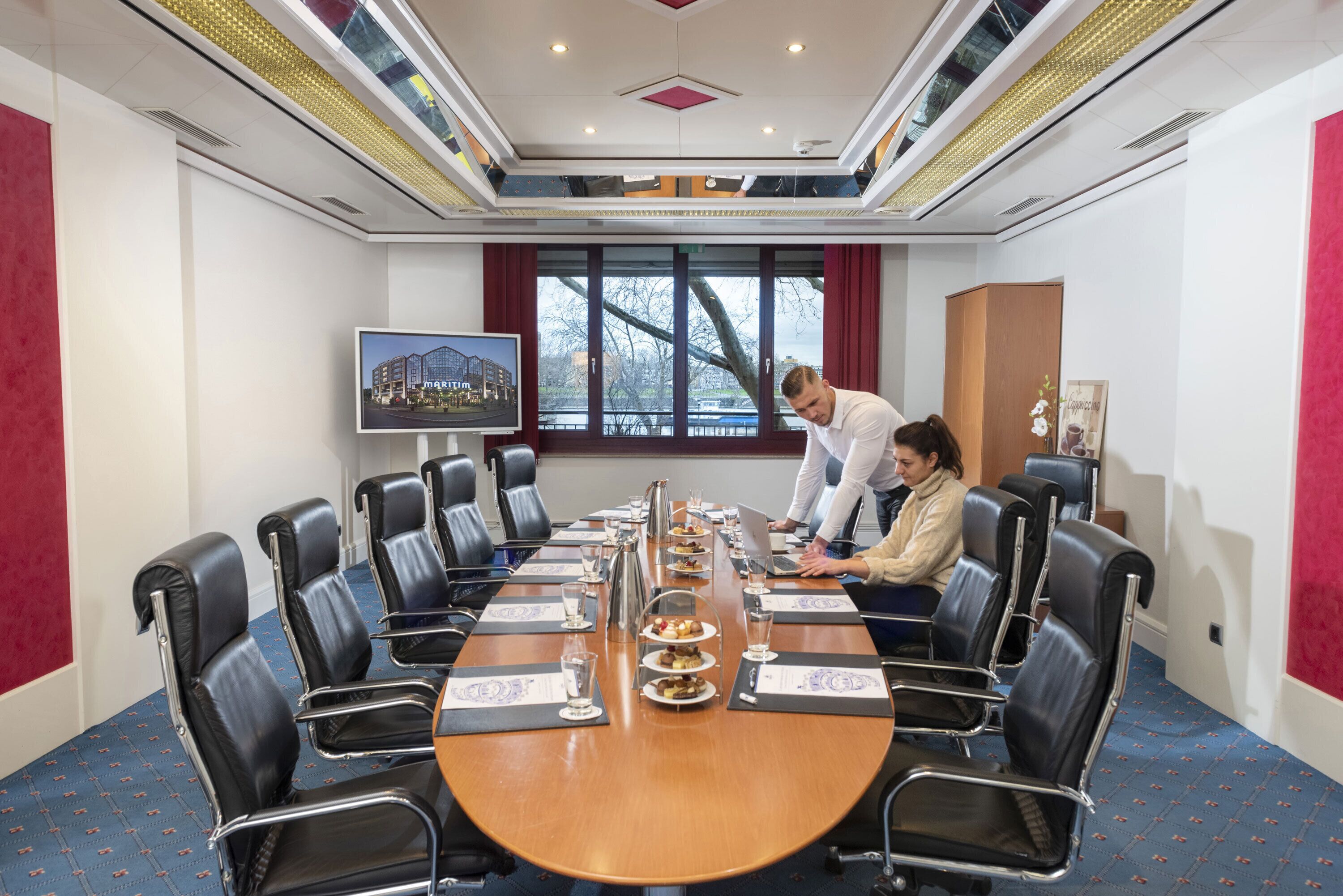 A conference room with a long table, black leather chairs, and a large window.