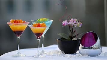 Zwei Martini-Gläser mit schichtweise Getränken und Garnituren, eine Topforchidee und eine spiegelnde Schale auf einem Tisch mit Eis.