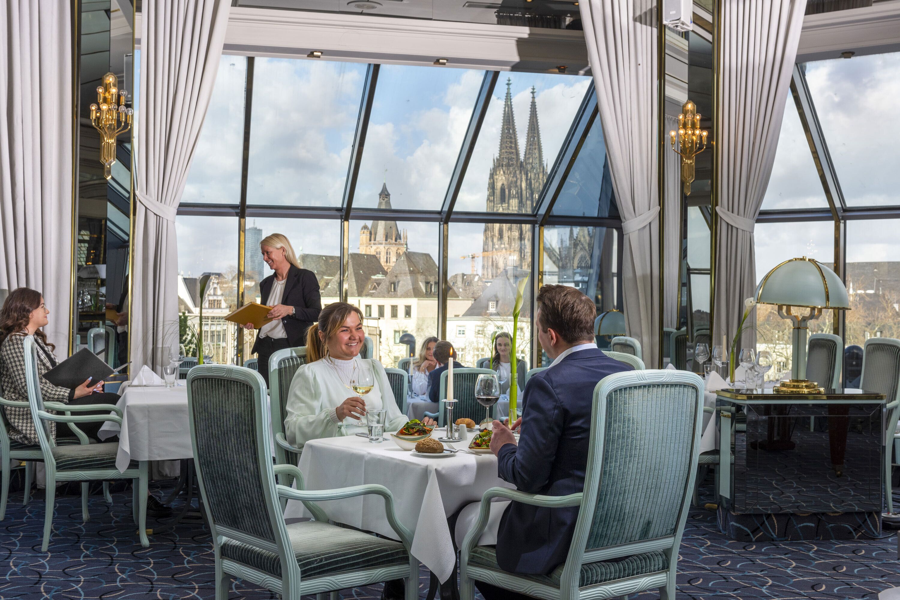 Un restaurant offrant une vue sur une cathédrale, des tables recouvertes de nappes blanches et des clients qui dînent.