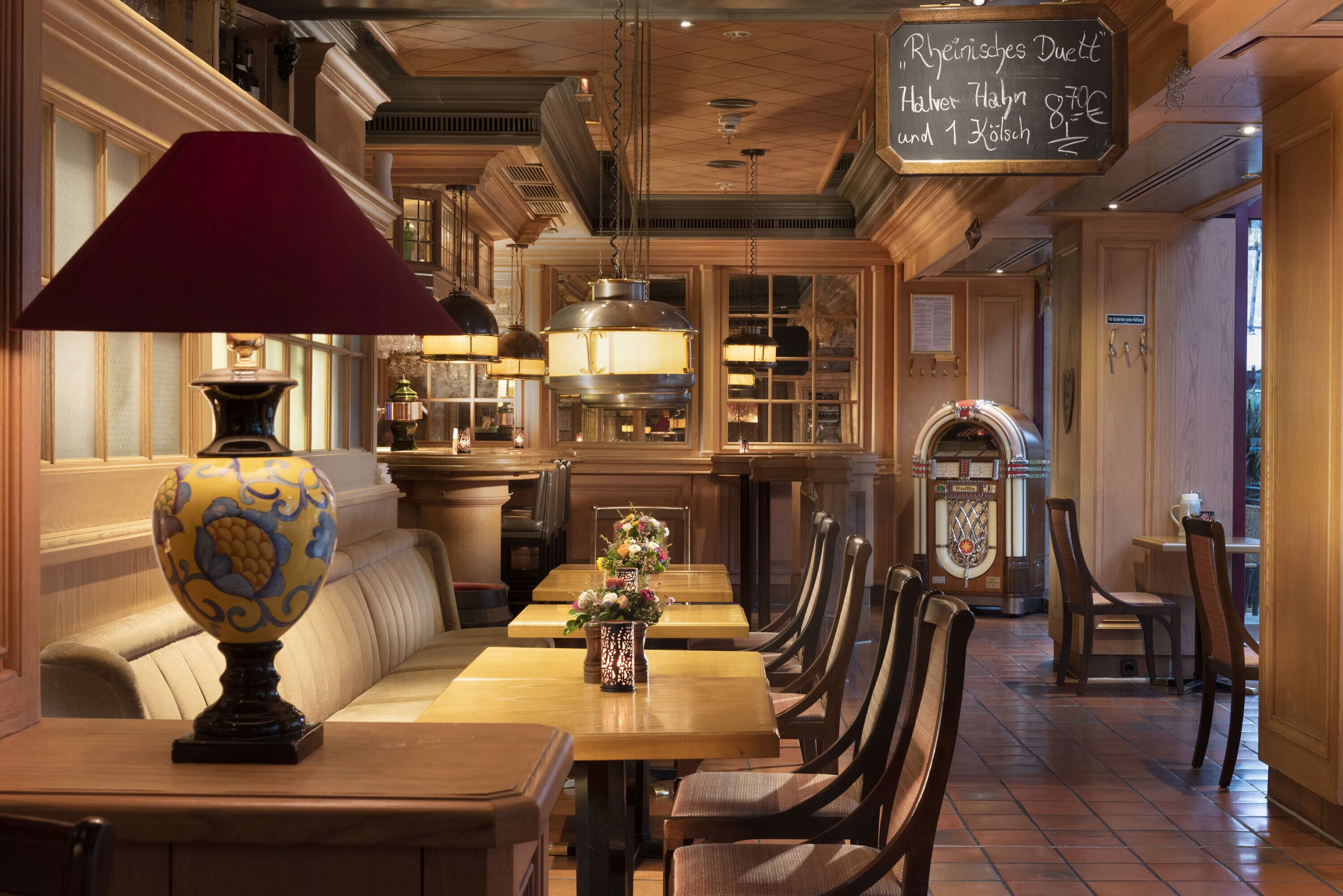 A restaurant with wooden tables and chairs, a decorative lamp, and a chalkboard menu.