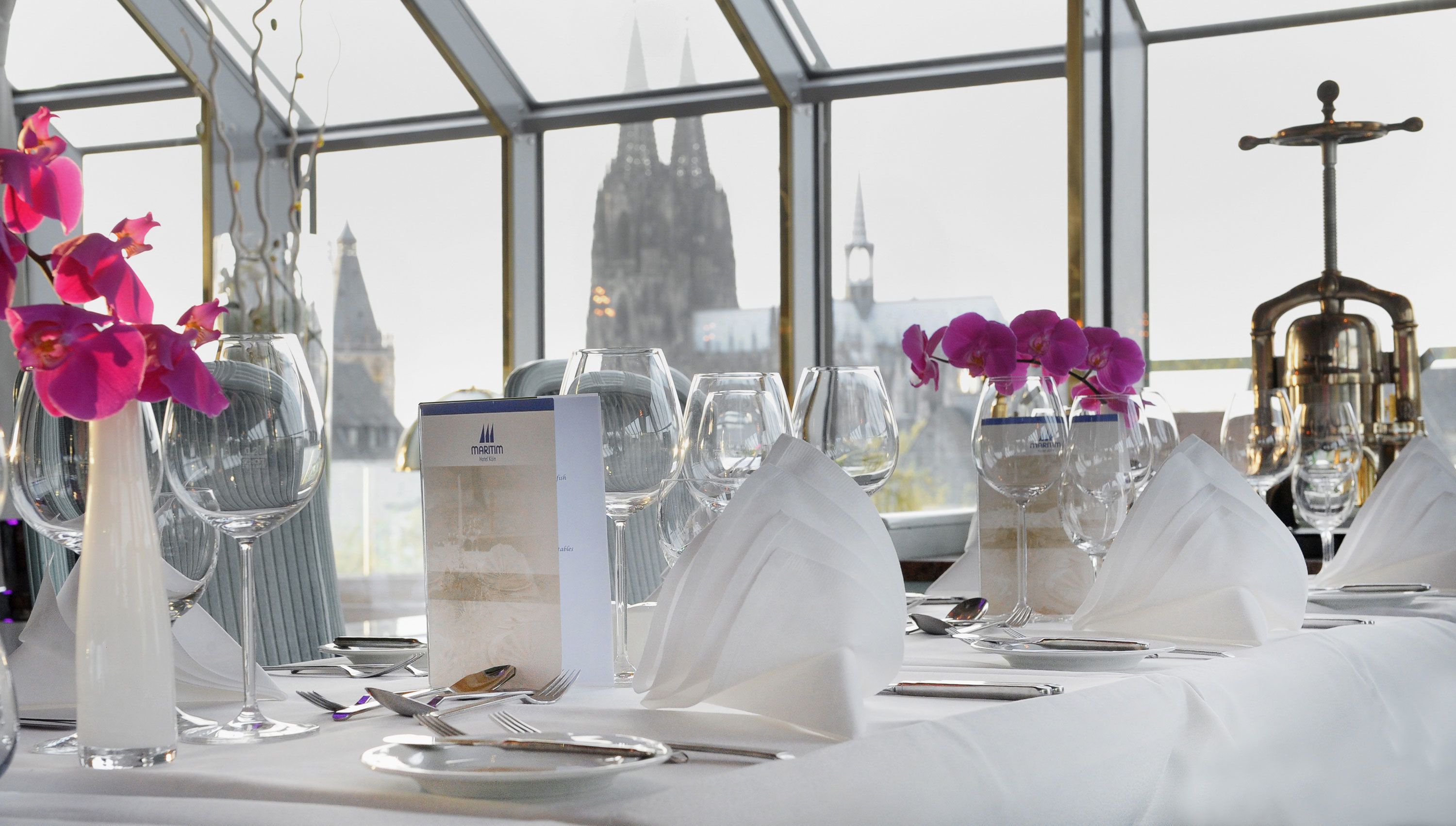 A table set for dining with a city view, including a church spire and a tower.