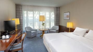 Habitación de hotel con una cama, dos sillones, un escritorio con televisor y dos lámparas.