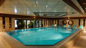 An indoor swimming pool with clear blue water, surrounded by lounge chairs and potted plants.