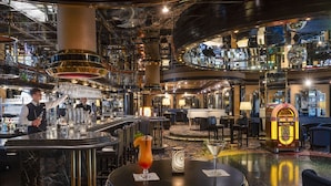 A bar area with a bartender, a round table with a drink, and a jukebox.