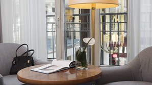 A modern room with a round wooden table, a lamp, a book, a vase with a plant, and a handbag.