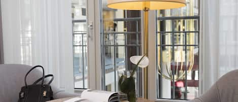 A room with a round wooden table, a lamp, a book, a handbag, and a vase with a flower.
