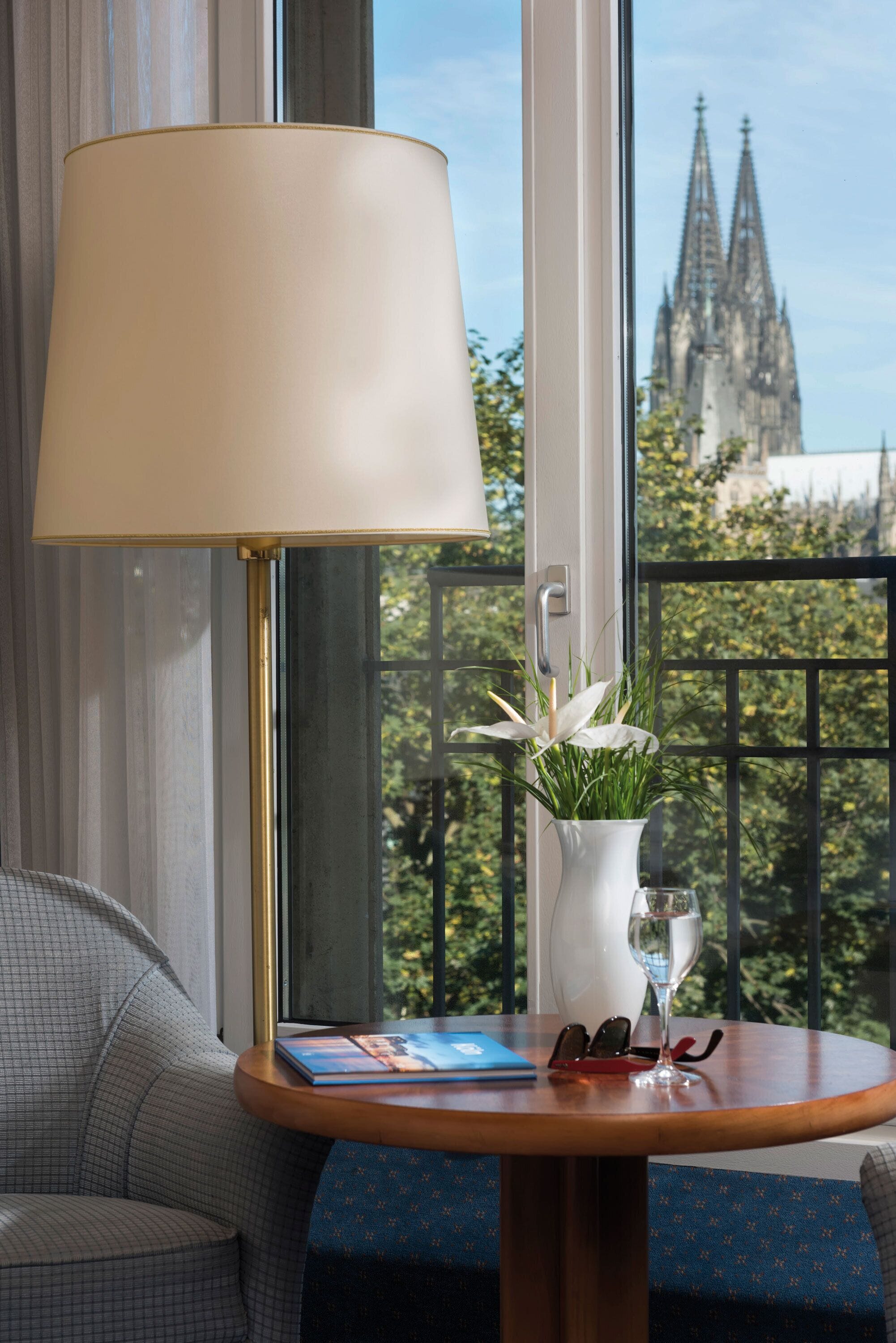 Ein Zimmer mit Tisch, Lampe, Blumenvase und Blick auf ein Dom.