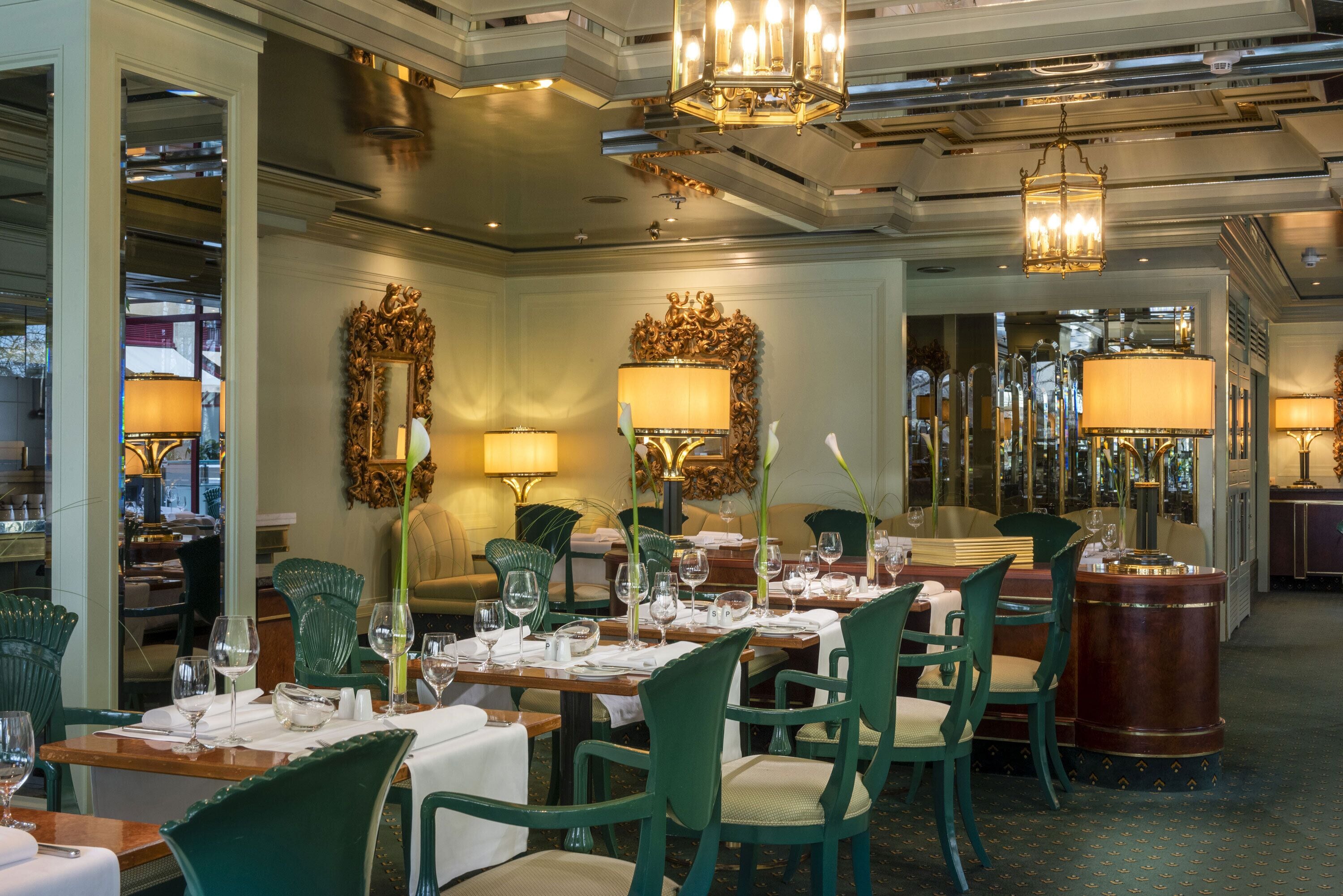 A dining area with green chairs, wooden tables, and chandeliers.