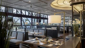 A modern restaurant with a high ceiling, large windows, and a central dining area with tables and chairs.