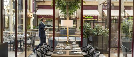 A restaurant with a glass enclosure, tables set with white tableware, and chairs with cushioned seats.