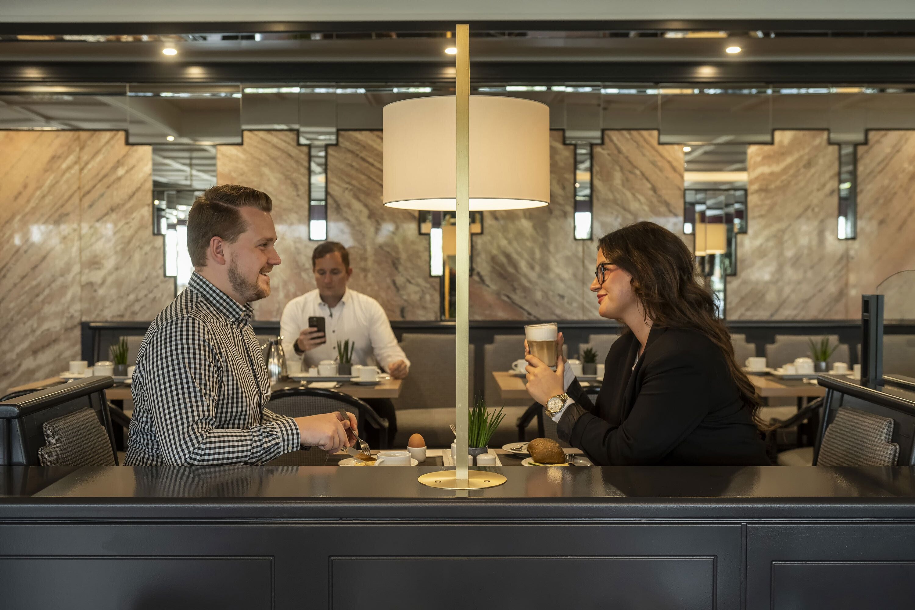 A modern restaurant setting with marble walls, a central table with a lamp, and diners engaged in conversation.