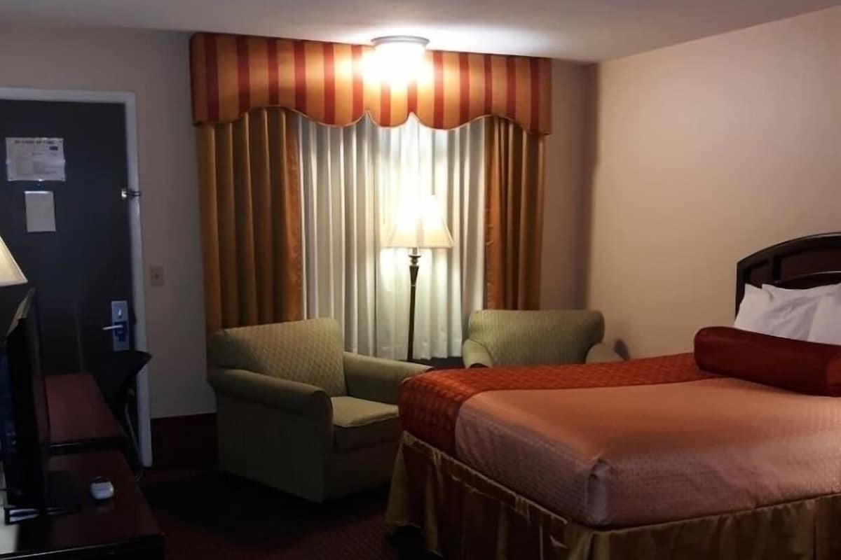 Una habitación de hotel con una cama, dos sillones, un escritorio y una lámpara.