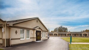 Een motel met een laag gebouw, een overdekte parkeerplaats en een gazon ervoor.