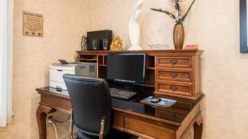 A business center with a desk, computer, printer, and a sign detailing hours and rules.