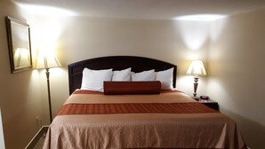 Een hotelkamer met een groot bed, twee bedlampjes, een nachtkastje met een klok en een lijst aan de muur.