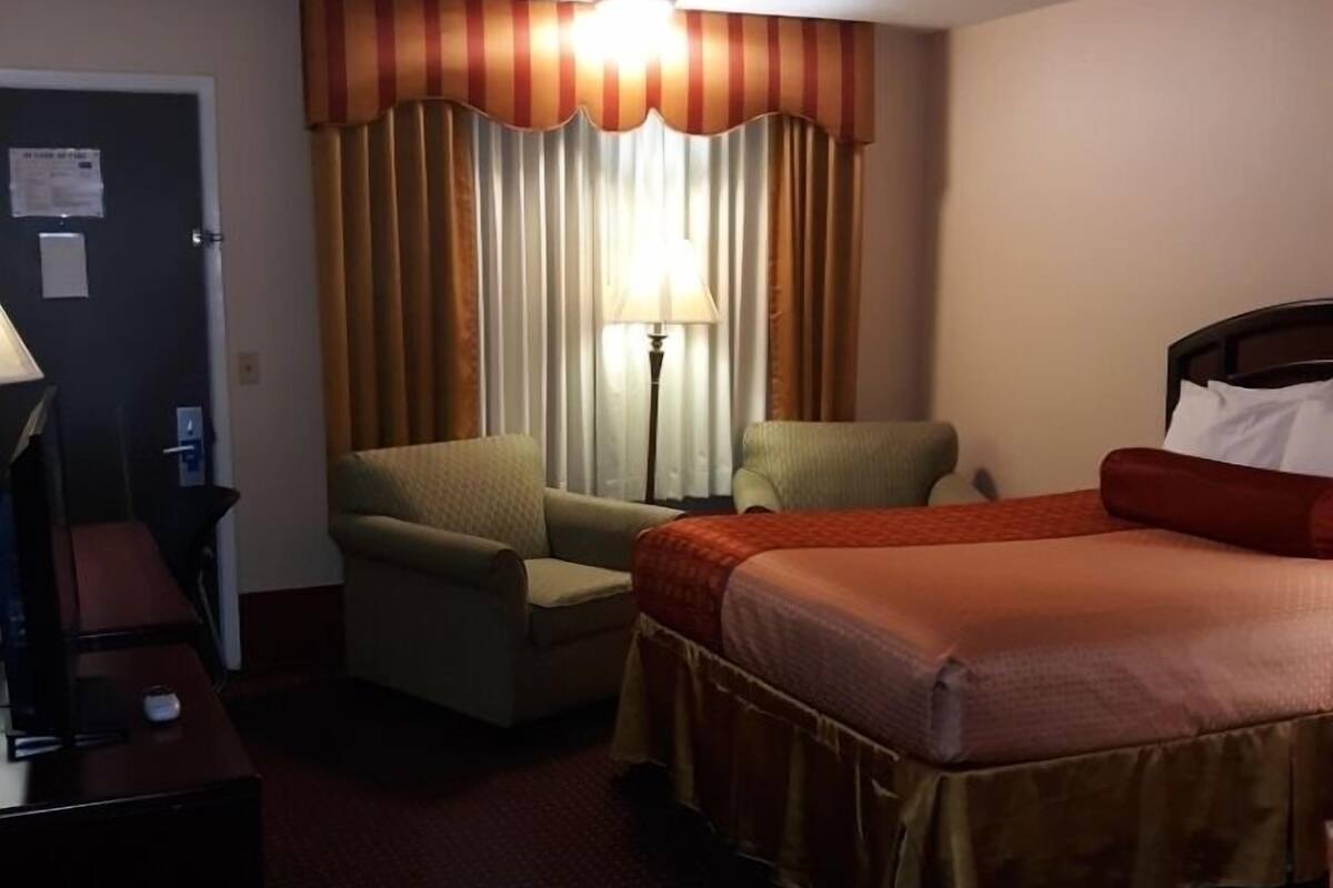 Ett hotellrum med en säng, två fåtöljer, ett skrivbord med en lampa och ett fönster med gardiner.