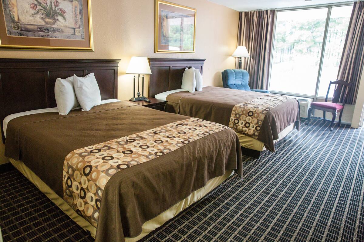 Une chambre d’hôtel avec deux lits, une grande fenêtre avec des rideaux, une chaise et une lampe.