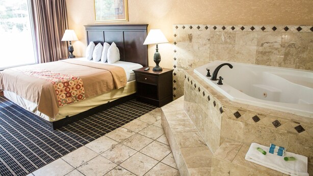 Habitación de hotel con una cama grande, baño independiente con bañera y ventana con cortinas.