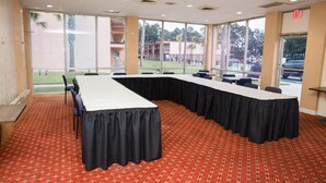 Un salón de conferencias con una larga mesa, sillas y ventanas amplias que ofrecen vistas al exterior.