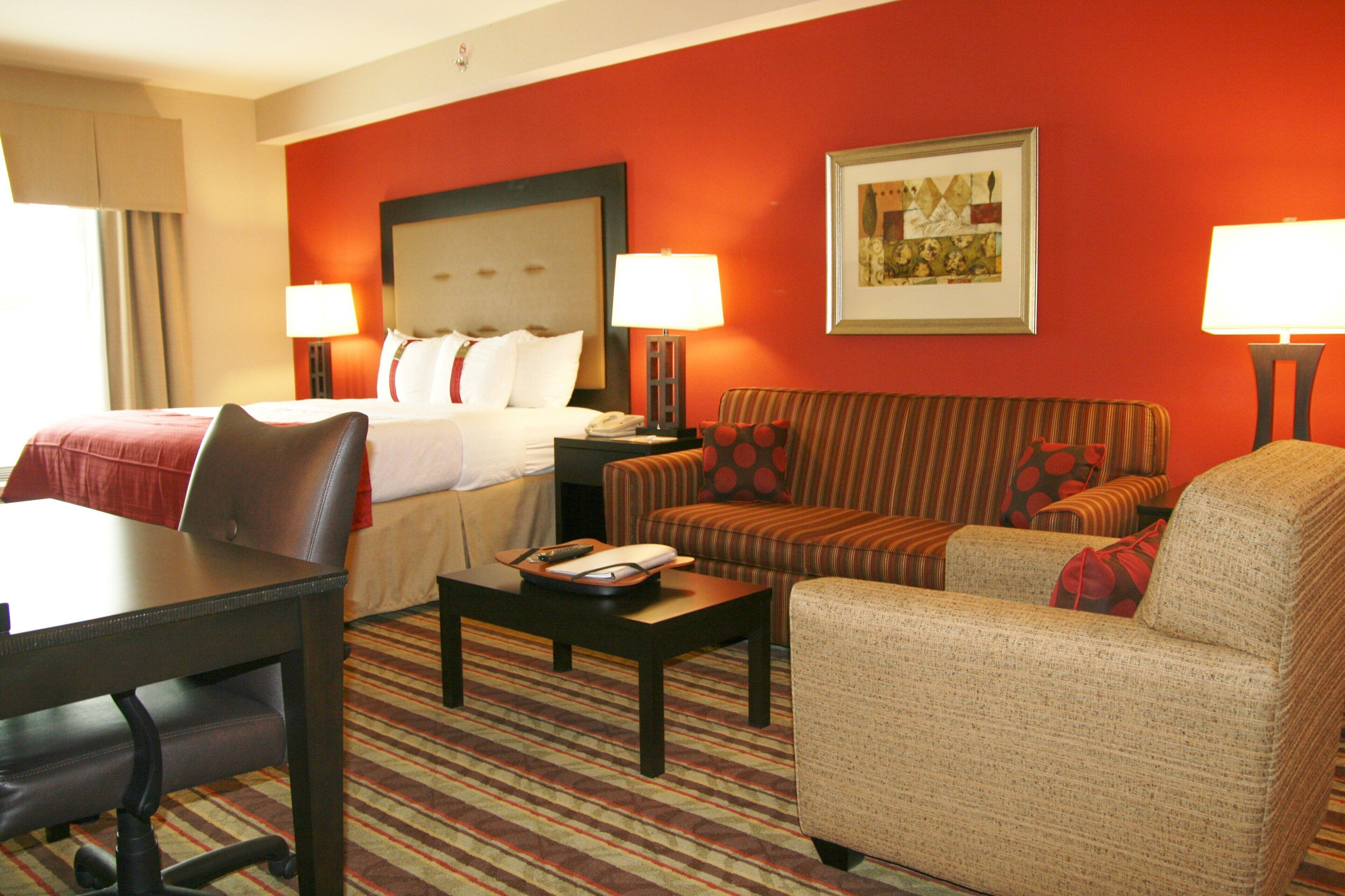 A hotel room with a bed, two armchairs, a sofa, a desk, and two bedside lamps.