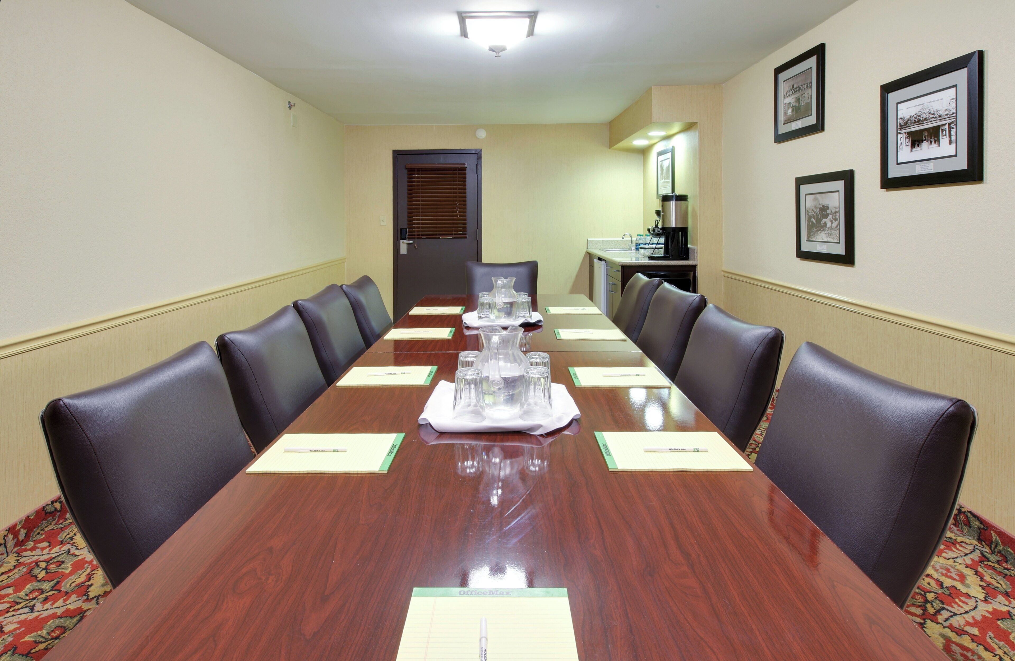 Uma sala de conferências com uma mesa comprida, cadeiras, um espaço para café e quadros nas paredes.