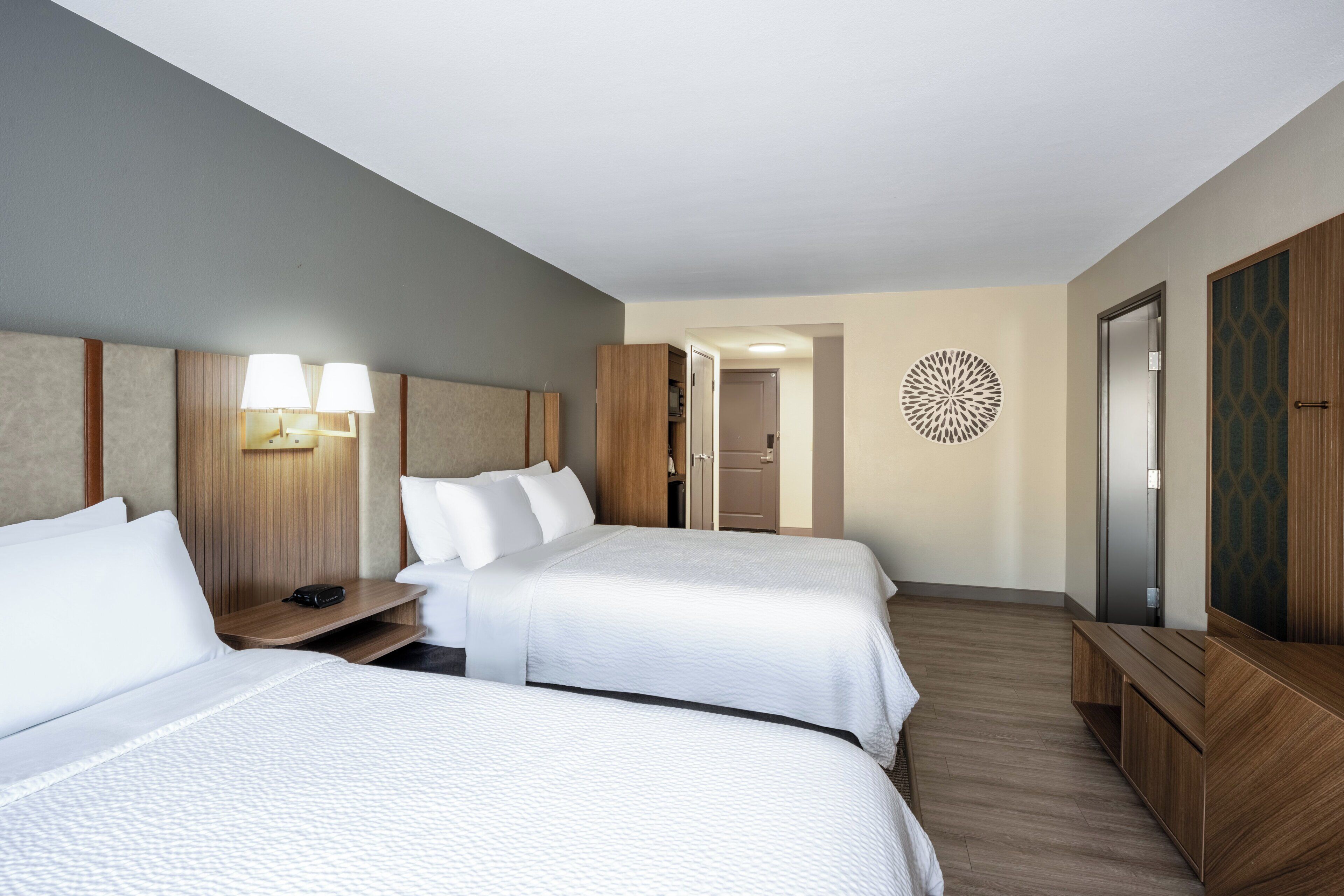 Habitación de hotel con dos camas, un escritorio, un armario y un adorno en la pared.