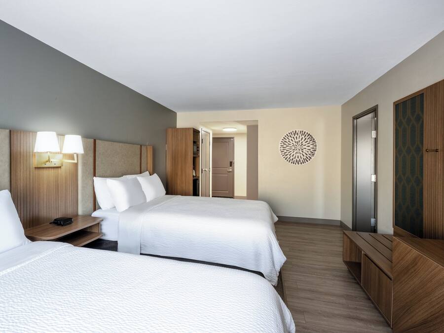 Habitación de hotel con dos camas, un escritorio, un armario y un adorno en la pared.