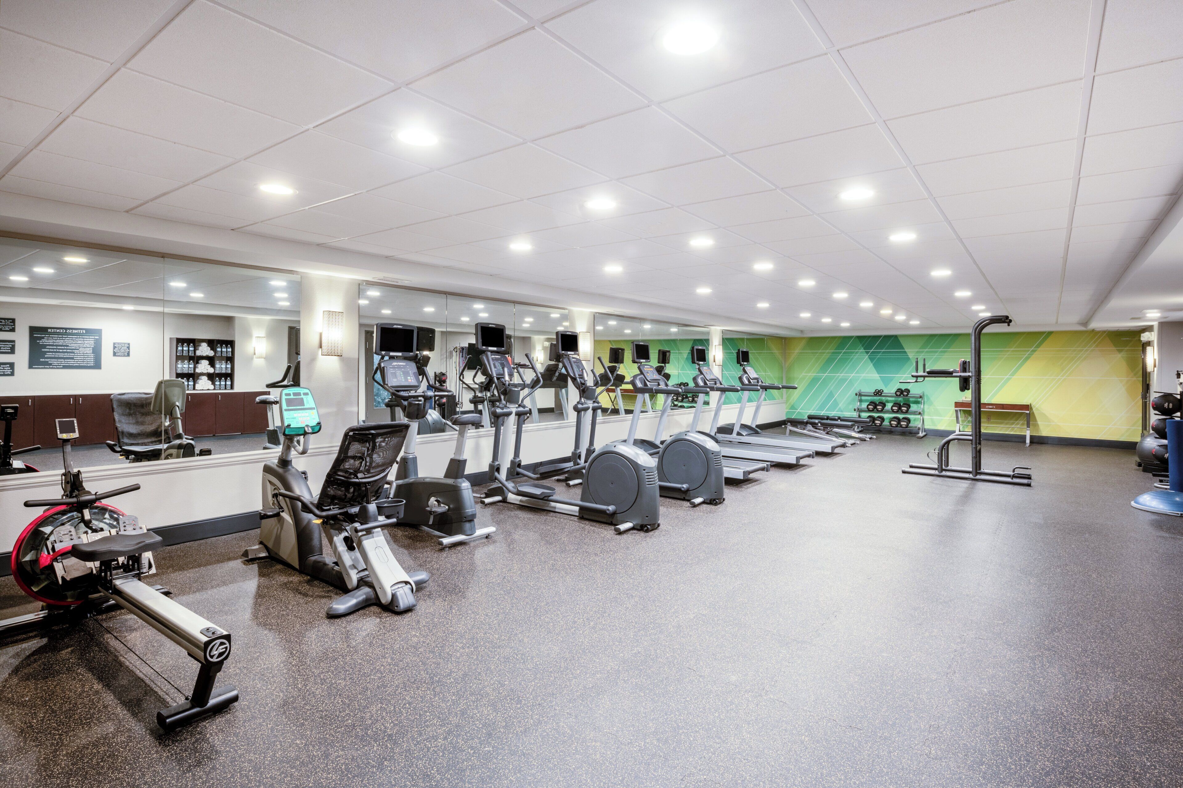 Ein Fitnessraum mit verschiedenen Trainingsgeräten, darunter Laufbänder und Ergometer, sowie einer Spiegelwand.