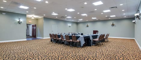 Un salón de conferencias con alfombra estampada, mesas con sillas e iluminación empotrada.