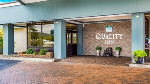 The exterior of a hotel with a brick pathway leading to the entrance, a sign reading "QUALITY INN", and potted plants at the entrance. - Quality Inn Oneonta Cooperstown Area (Oneonta)