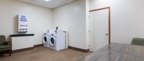 Une pièce comprenant une grande table, un lave-linge, une chaise et une porte.