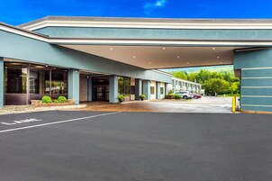Una entrada de hotel moderna con un vestíbulo cubierto, amplias ventanas y un área de estacionamiento.