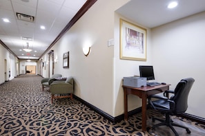 A hotel hallway with patterned carpet, a desk with a computer, and framed artwork on the wall. - Quality Inn Oneonta Cooperstown Area (Oneonta)