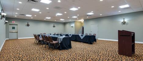 Une salle de conférence avec des tables disposées pour une réunion, un pupitre et un panneau indiquant la sortie.