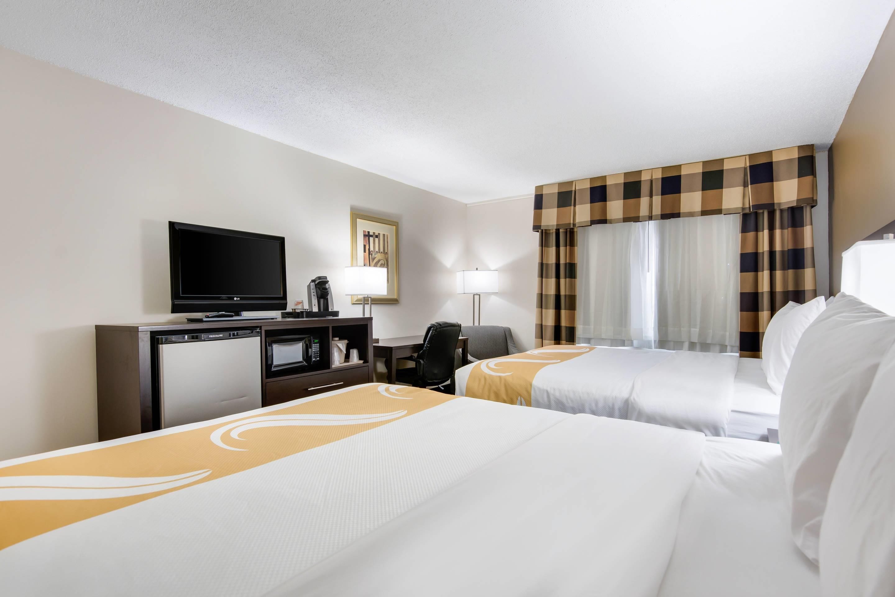 Habitación de hotel con dos camas, televisión, escritorio con computadora y ventana con cortinas.