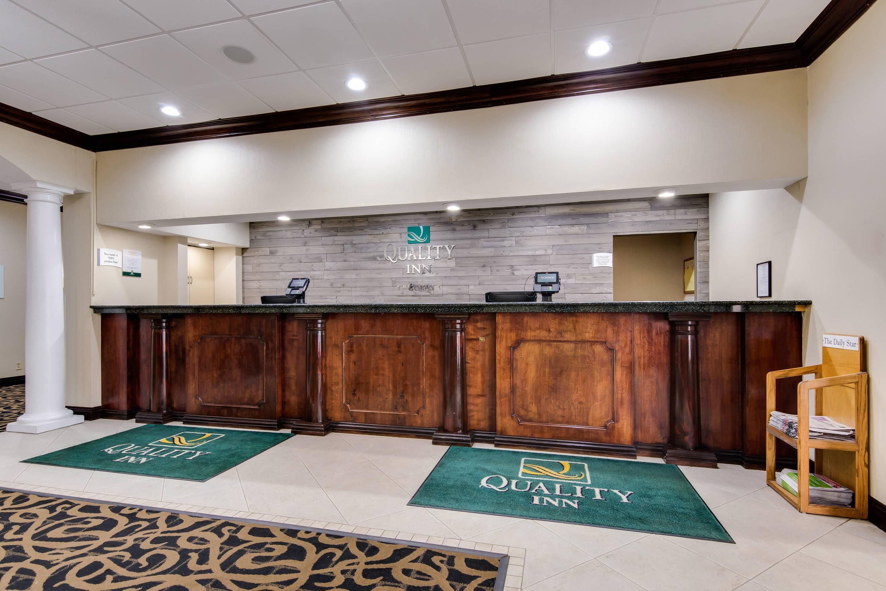 A reception area with a wooden counter, a sign reading "Quality Inn," and a reception desk.
