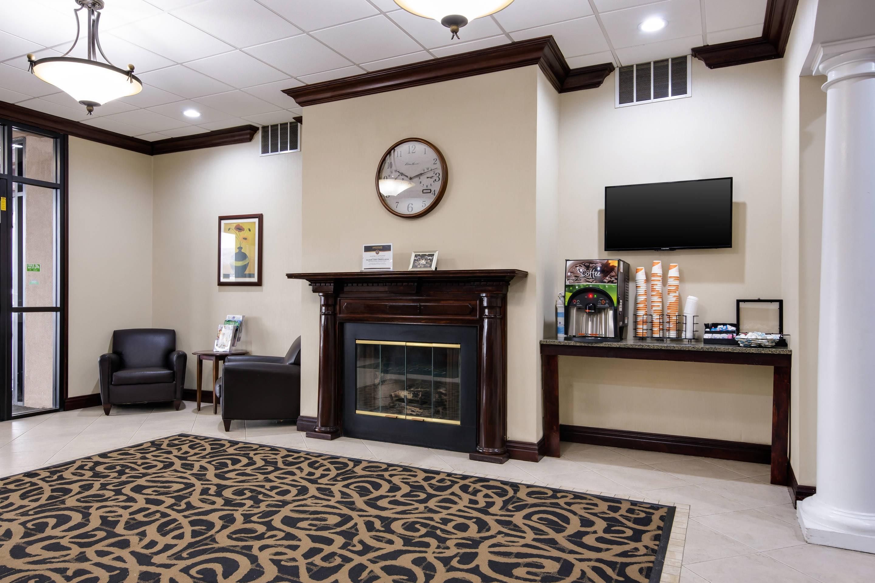 A lobby with a fireplace, a clock, a television, and a coffee station.