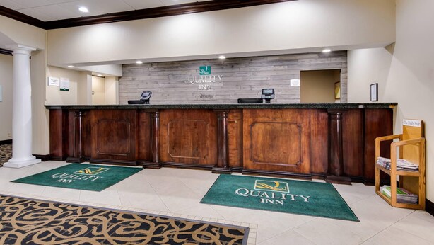 A reception area with a wooden counter, a sign reading "Quality Inn," and a reception desk. - Quality Inn Oneonta Cooperstown Area (Oneonta)