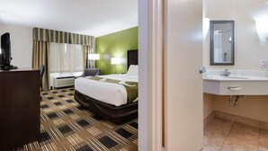 A hotel room with a bed, bedside lamps, a desk, and a bathroom with a sink and mirror. - Quality Inn Oneonta Cooperstown Area (Oneonta)