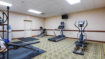 A fitness room with treadmills, elliptical machines, and a bench.