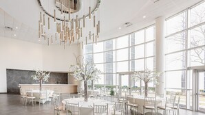 Un comedor amplio con mesas redondas, sillas blancas y ventanas grandes que ofrecen vistas al exterior.