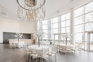 A spacious dining area with round tables, white chairs, and large windows offering views of the outdoors.