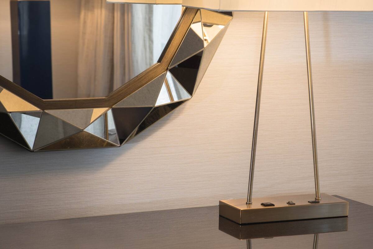 A modern hotel room with a geometric-patterned mirror, a contemporary lamp, and a blue chair.