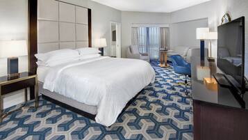 Une chambre d’hôtel avec un grand lit, un bureau, une chaise, une télévision et une fenêtre avec des rideaux.