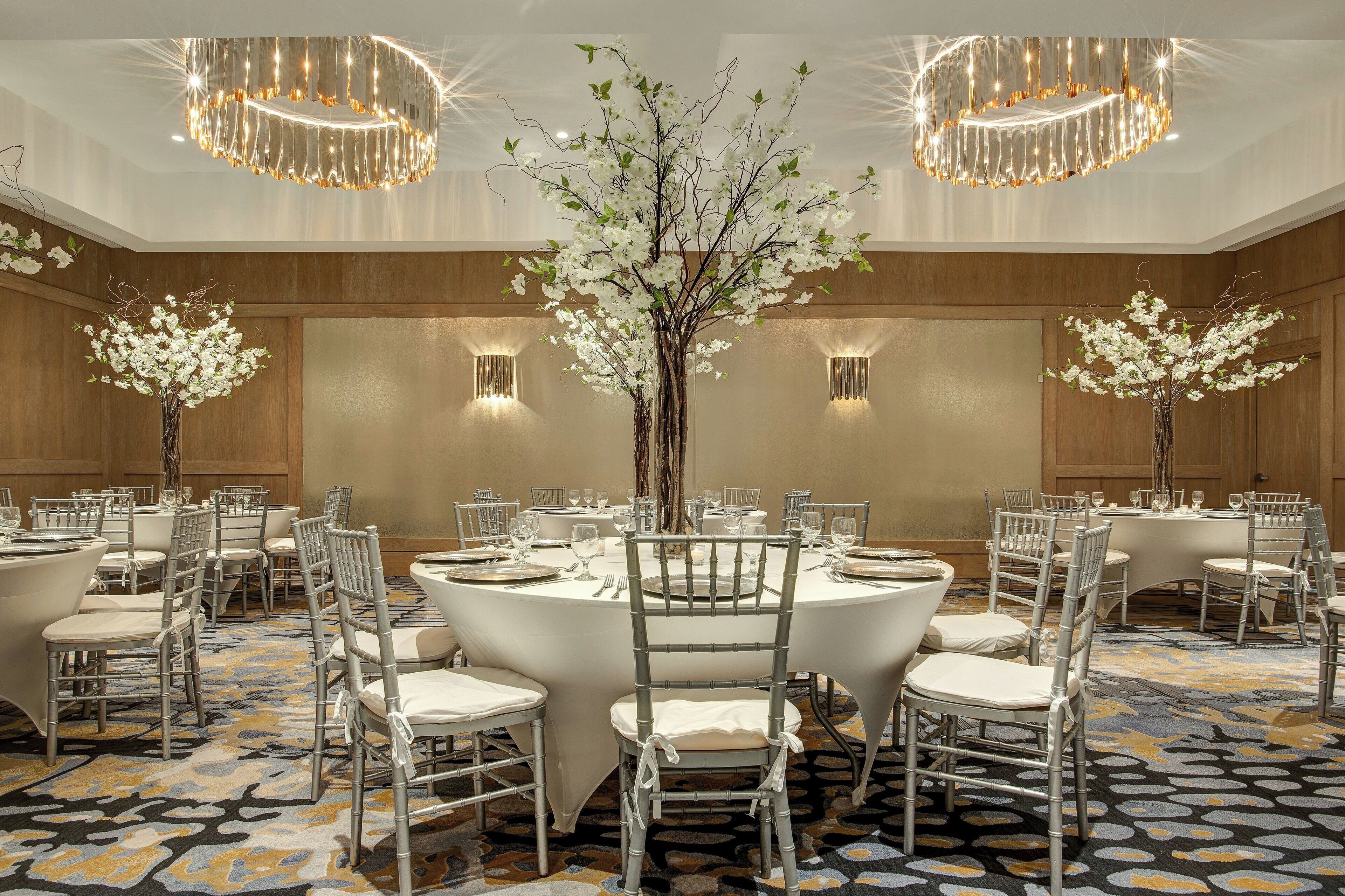 A banquet hall with round tables, white chairs, and floral centerpieces.