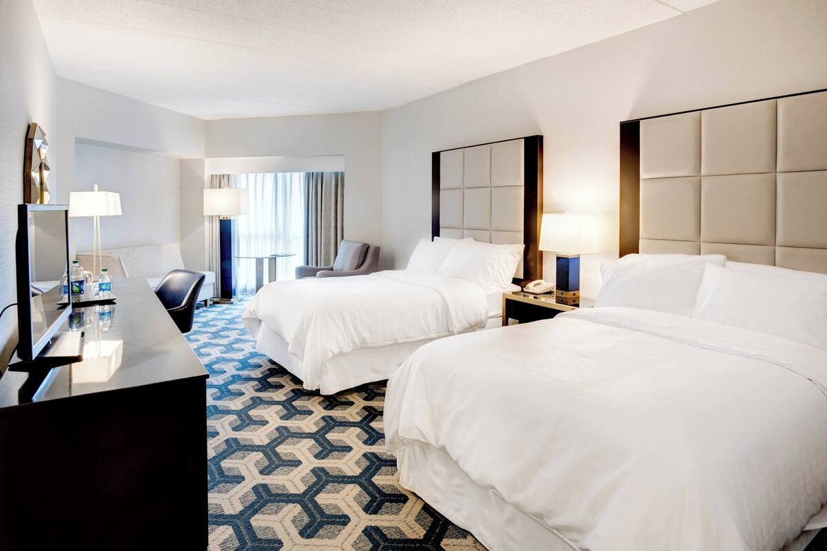 A hotel room with two beds, a desk, and a chair.