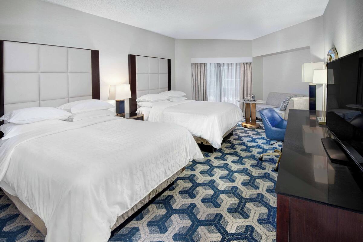 A hotel room with two beds, a desk, a chair, and a TV.