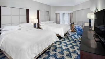 A hotel room with two beds, a desk, a chair, and a TV.