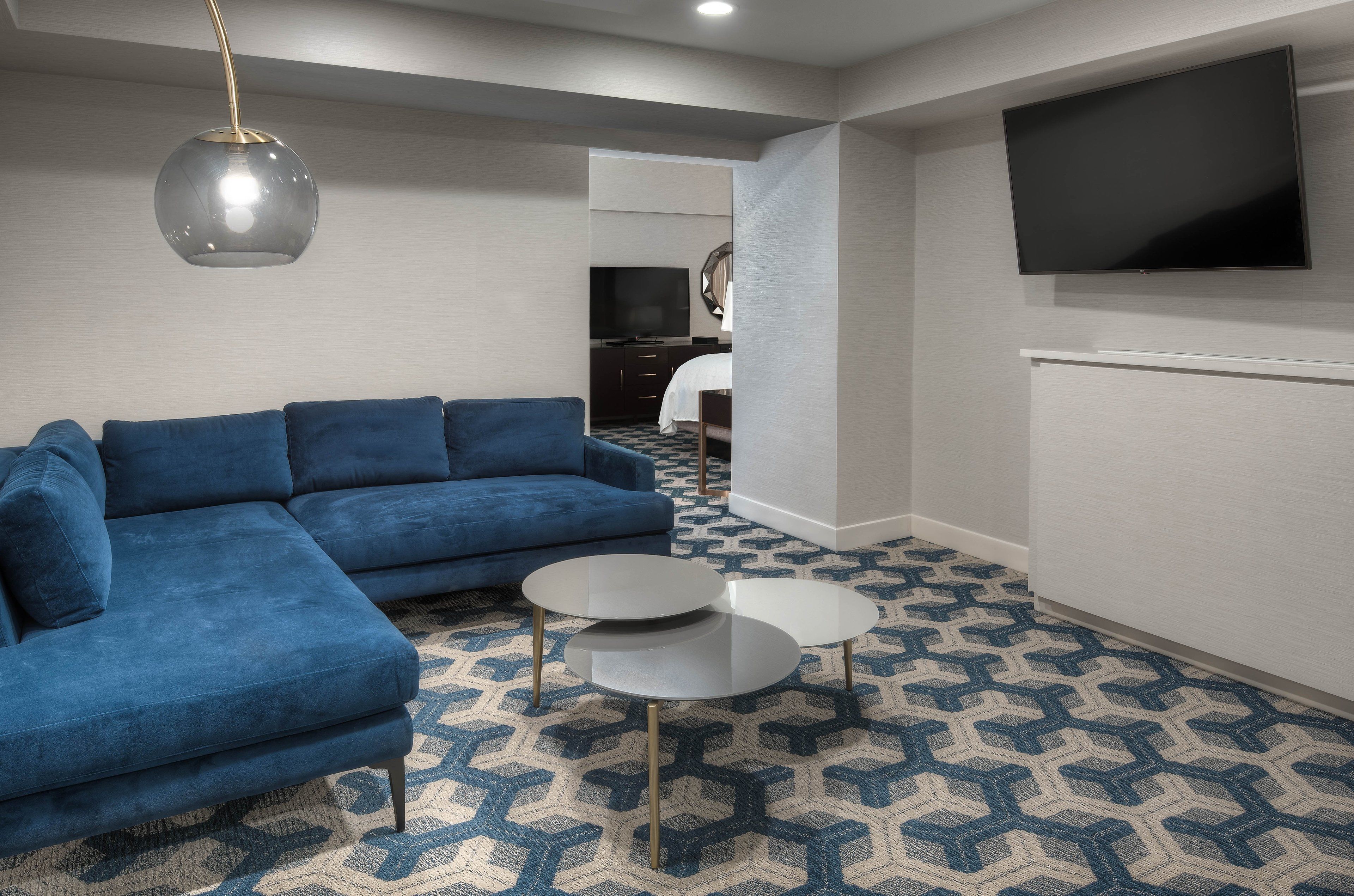 Una sala de estar moderna con un sofá seccional azul, dos mesas de centro redondas y una alfombra estampada.