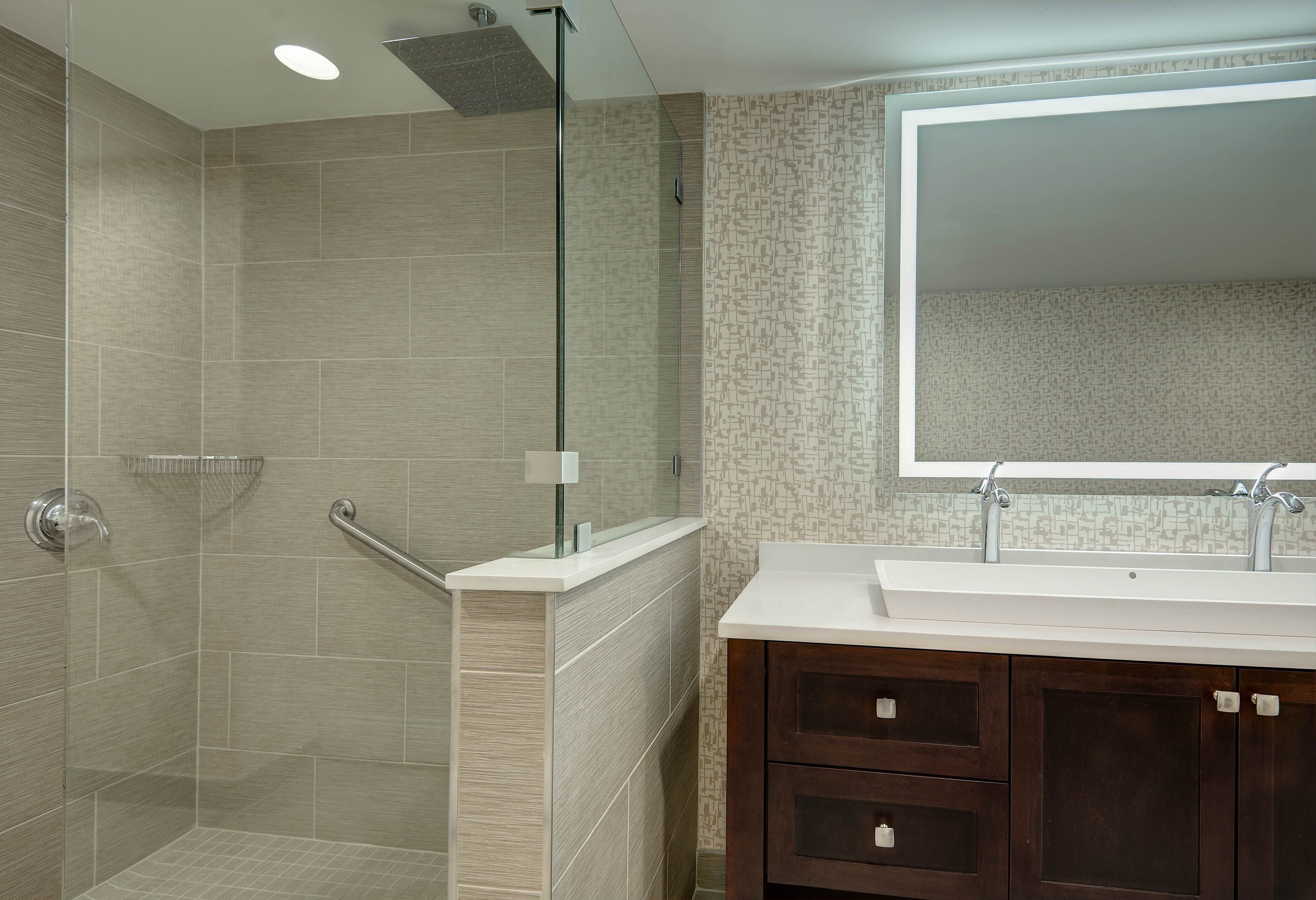Une salle de bain moderne équipée d’une douche, d’un meuble-lavabo et d’un grand miroir.